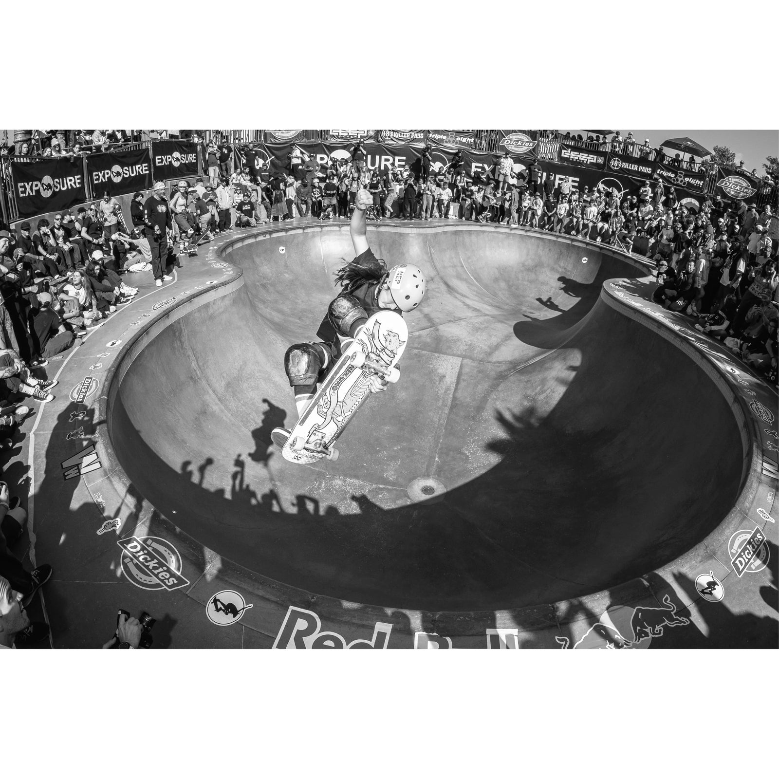 A black and white photo of a woman skateboarding in a skate pool surrounded by a crowd.