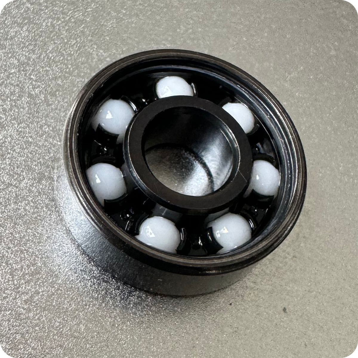 A close-up of a black HST FAF BEARINGS by Art Function with white ceramic balls rests on a textured metallic surface, showcasing the precision and quality of these high-performance bearings.