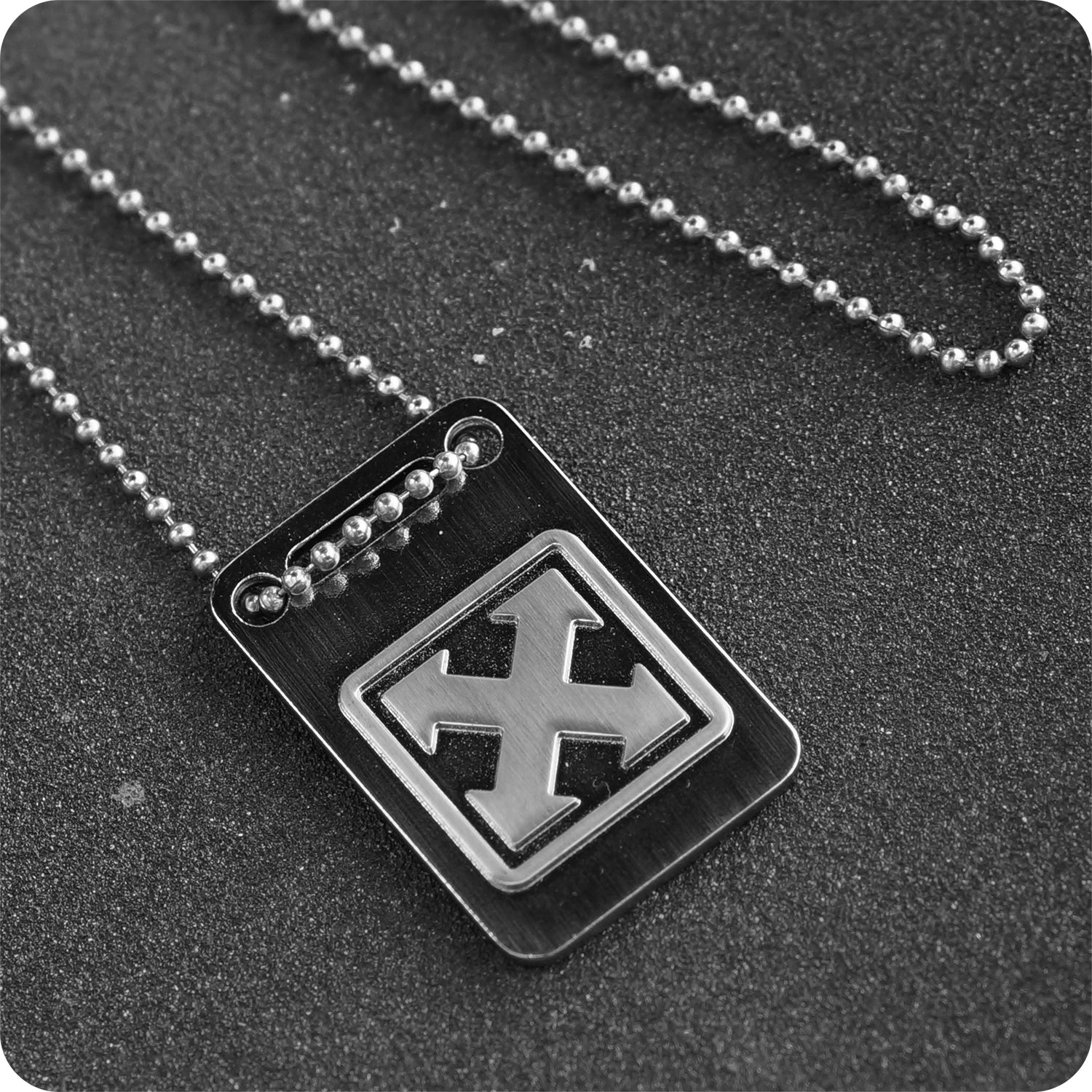 The 5TH DAY OF CHRISTMAS PACKAGE 2024 by H-Street Skateboards features a metallic dog tag necklace with a raised X design, inspired by original re-issue graphics, displayed on a textured dark surface.