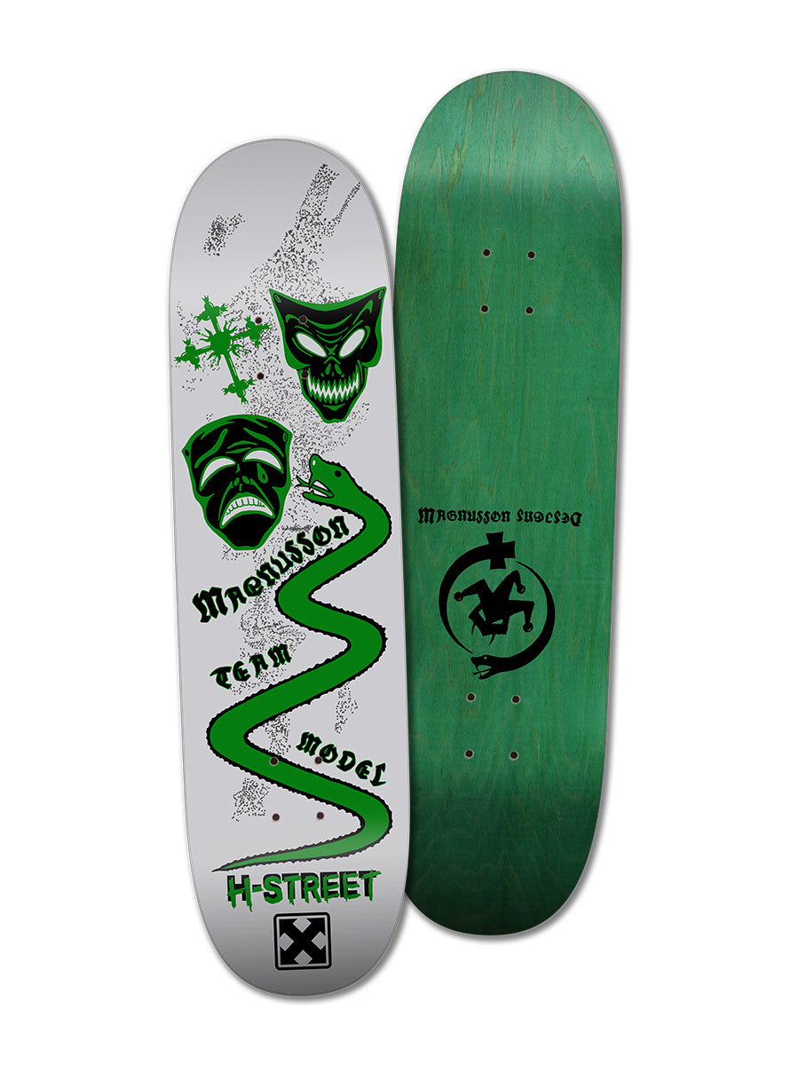 Two skateboard decks: one with green wood grain and black Magnusson Designs logo, the other is a Woodchuck T-MAG MASKS & SERPENT deck in gray with green and black skulls, splatters, winding line, and Magnusson Team Model text.