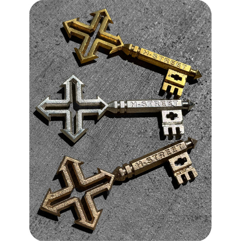 Three metal keys with 'H-STREET' inscribed on them, displayed in bronze, silver, and gold colors.