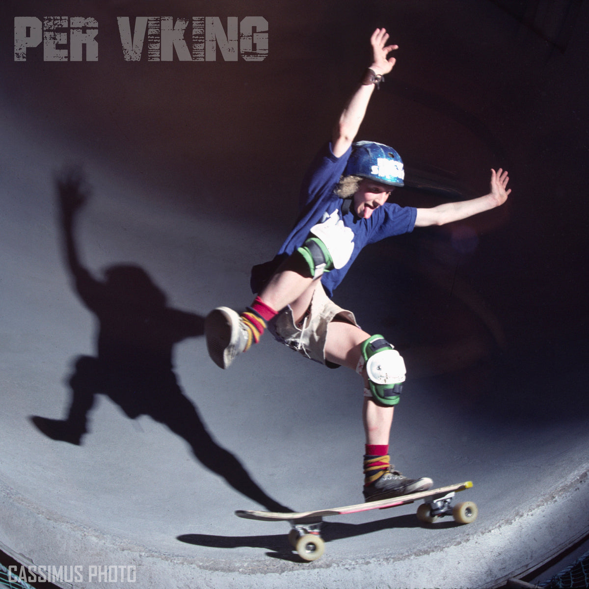 A skateboarder in a blue shirt and helmet performs a trick on a curved ramp in Vällingby under dramatic lighting. His shadow appears on the ramp wall. Text reads PER VIKING MEMORIAL SERIES by Woodchuck, celebrating his skateboarding legacy.