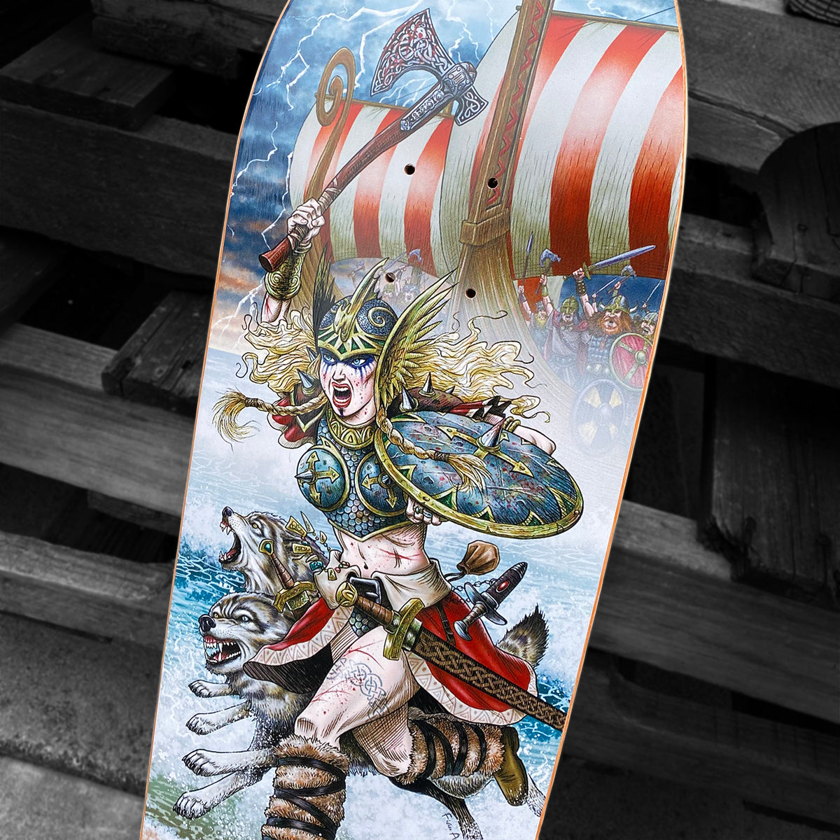 The Woodchuck PER VIKING MEMORIAL SERIES skateboard deck showcases a fierce Viking woman with helmet, shield, and axe, flanked by wolves, amid stormy seas with Vällingby’s spirit joining Viking ships and warriors.