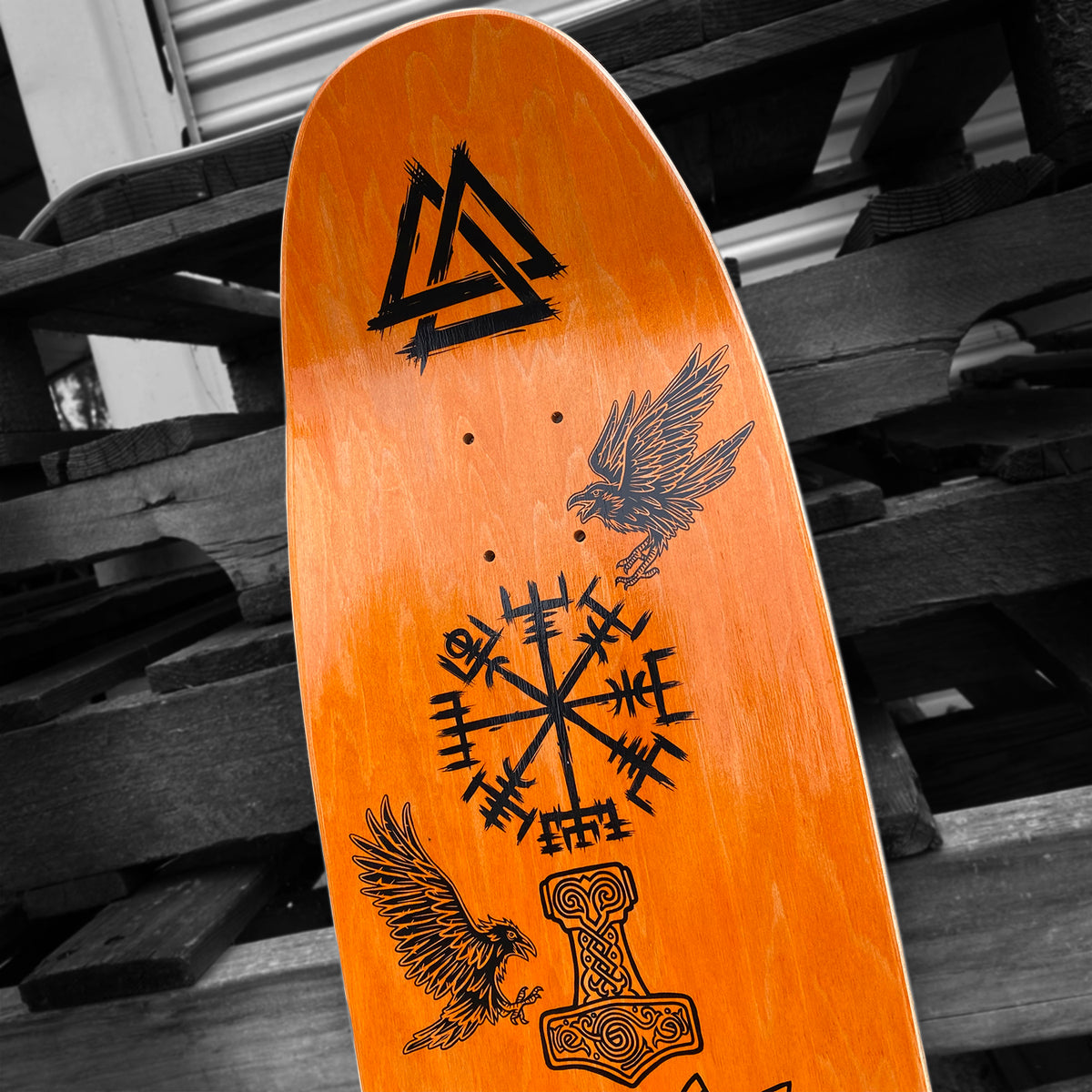 The Woodchuck PER VIKING MEMORIAL SERIES skateboard deck features striking Norse-inspired black art—ravens, Vegvisir, a hammer, and knot—set on vibrant orange wood, showcasing Vällingby Viking designs.
