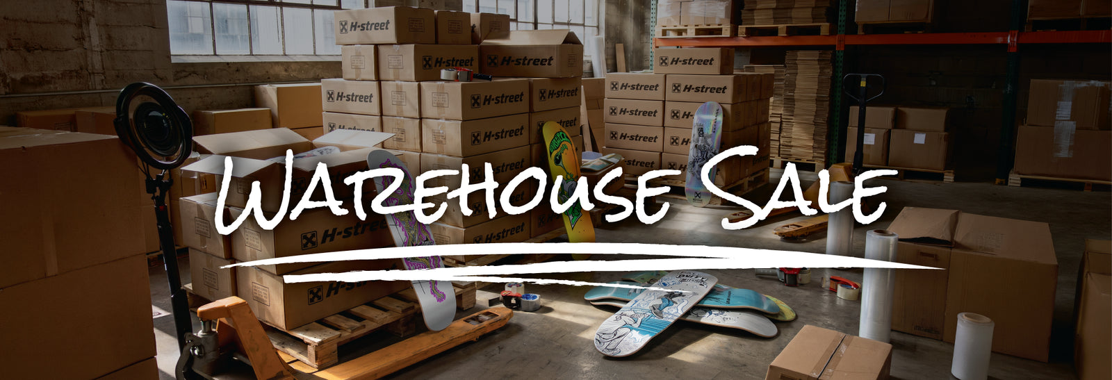 An image of a warehouse filled but H-Street labeled boxes and skateboard decks scattered around with the words 'Warehouse Sale' on top.