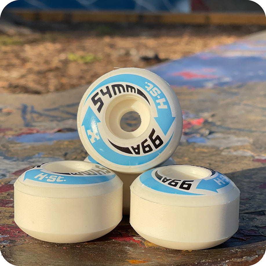 Three white PriPro Polymers H-STREET LOGO WHEELS, 54mm 99A, stack on a painted skatepark in sunlight—high rebound urethane wheels ideal for your next session.