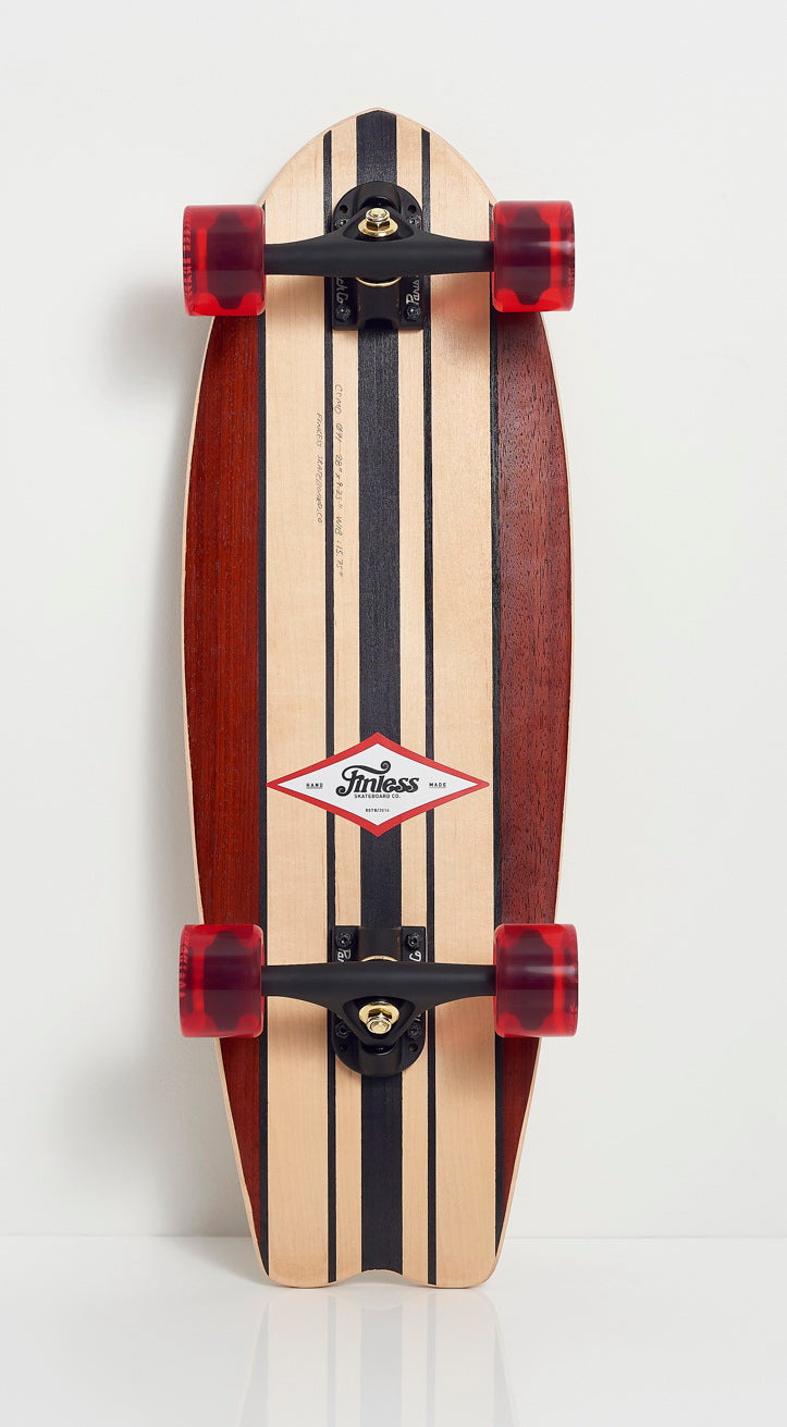 The FINLESS COMPLETE by Finless is a handcrafted longboard with a wooden deck in black and dark brown stripes, red transparent wheels, and black trucks, shown upright against a white background.