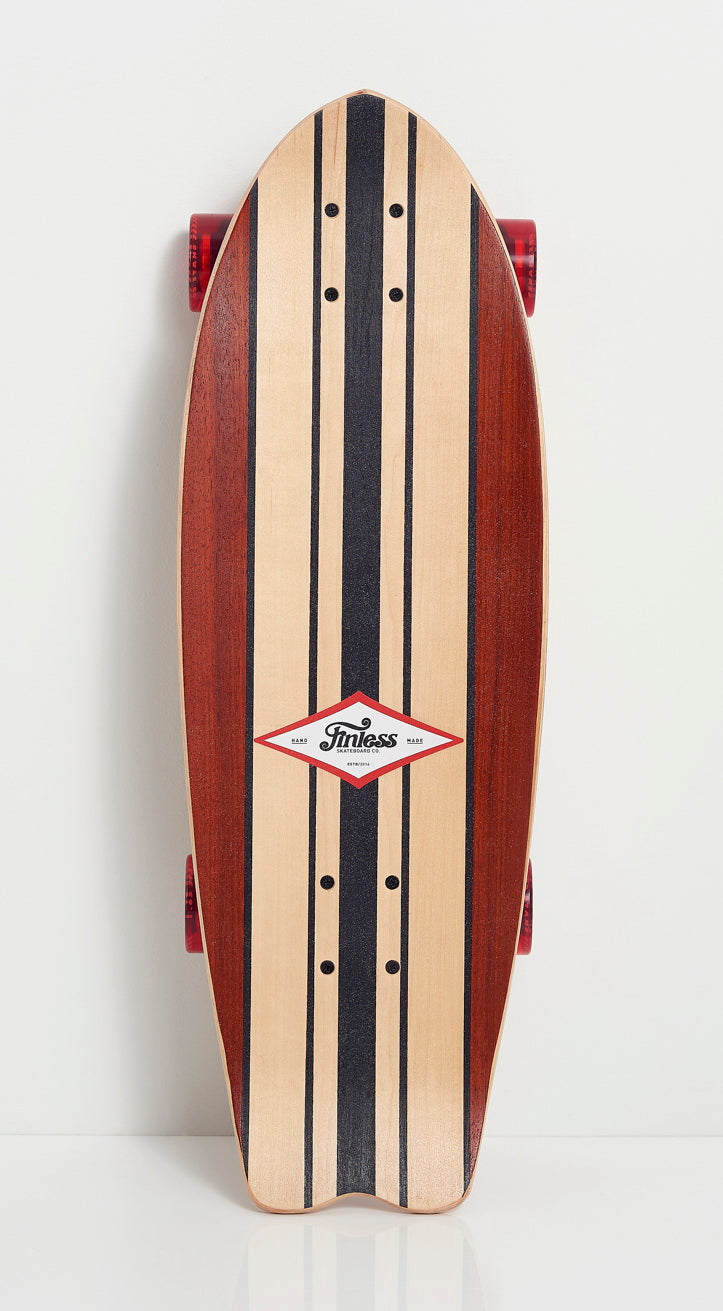 The FINLESS COMPLETE by Finless is a handcrafted longboard with red wheels, dark and light vertical stripes, and a diamond-shaped Tinkess Skate logo at the center, displayed on a plain white background.