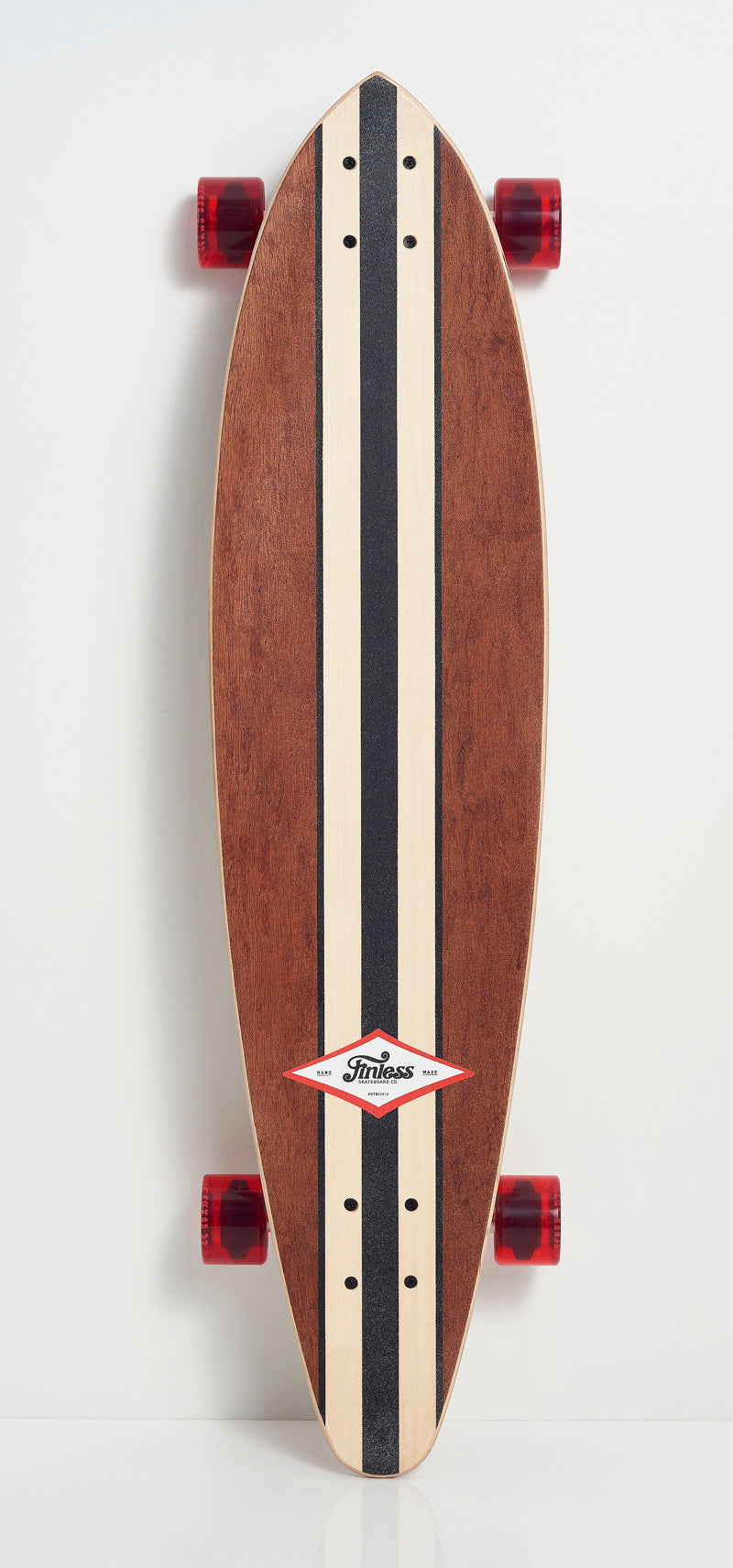 The FINLESS COMPLETE by Finless is a handcrafted longboard featuring a wood finish, black racing stripes, red wheels, and a Finless logo near the front. This retro surf skateboard stands upright against a plain white background.