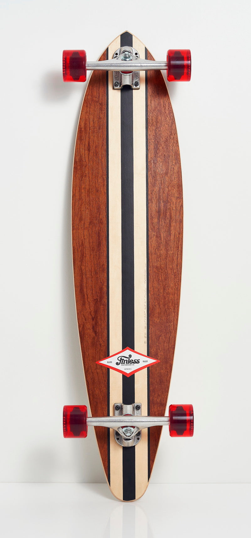 The Finless FINLESS COMPLETE skateboard by Finless features a wooden deck with black and cream racing stripes, red wheels, and metal trucks, standing vertically against a white background for classic cruiser style.