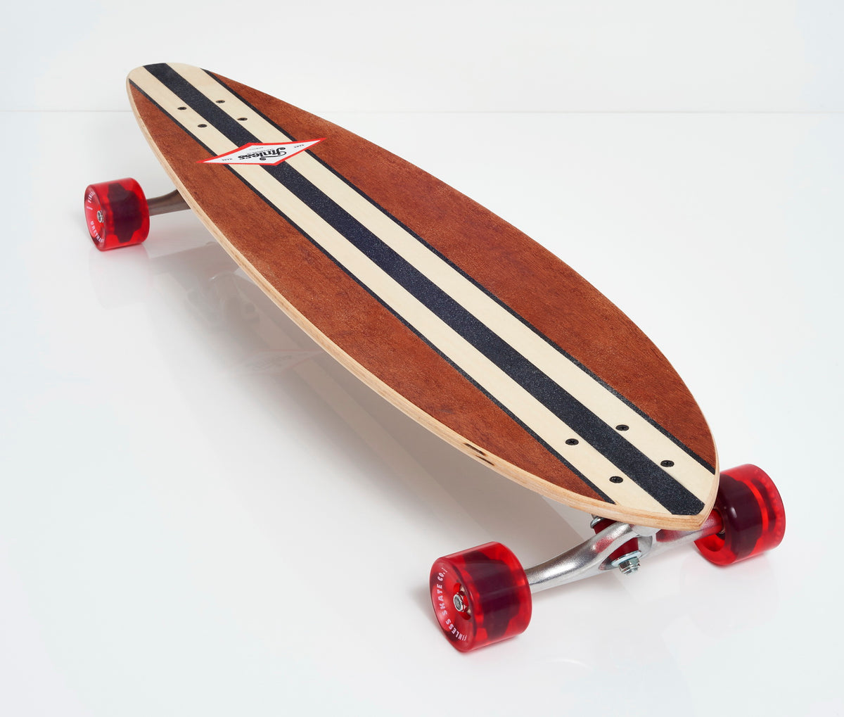 The Finless FINLESS COMPLETE is a hand crafted longboard by Finless featuring black and white center stripes, red wheels, and silver trucks. This retro surf skateboard is displayed on a white surface.