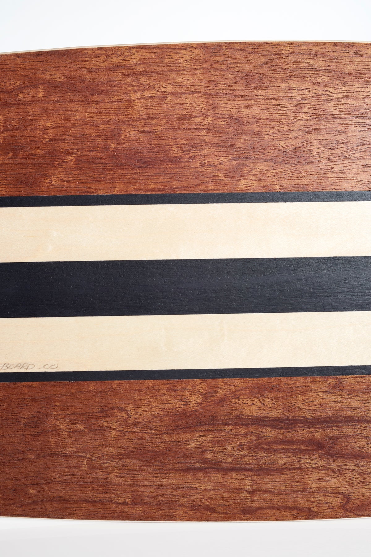 A close-up of the Finless FINLESS COMPLETE longboard by Finless, showcasing a wide cream stripe bordered by black stripes on a rich reddish-brown wood grain background.