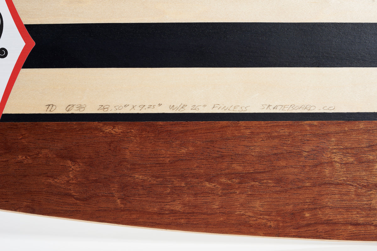 Close-up of the FINLESS COMPLETE by Finless, a retro surf skateboard deck with horizontal black and wood-grain stripes, featuring handwritten specs: 28.50” x 9.25”, W/B 15.25.