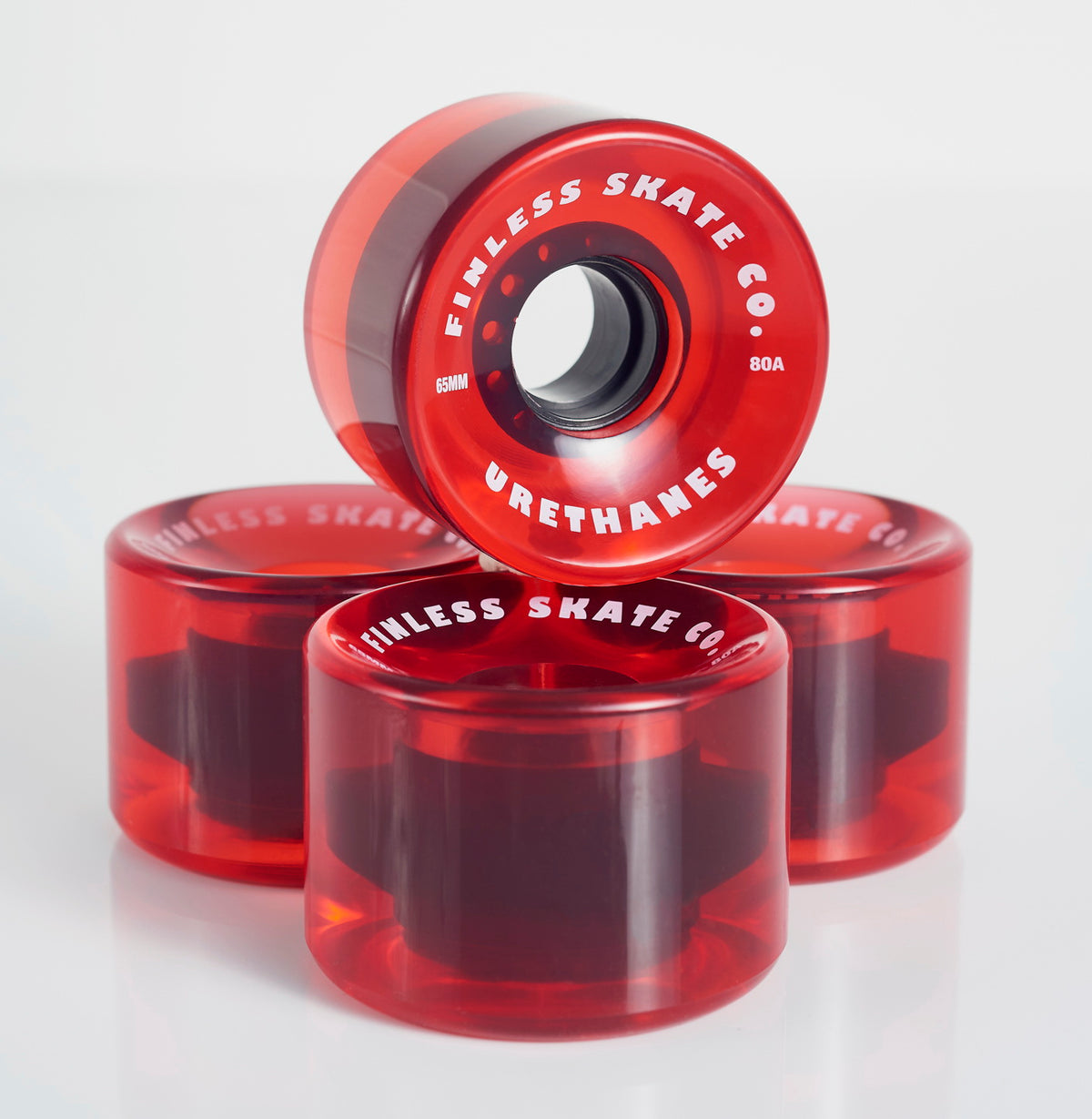 Four translucent red wheels from the Finless FINLESS COMPLETE set are stacked on a white surface, with one upright showing the Finless branding—ideal for cruiser boards or your retro surf skateboard setup.