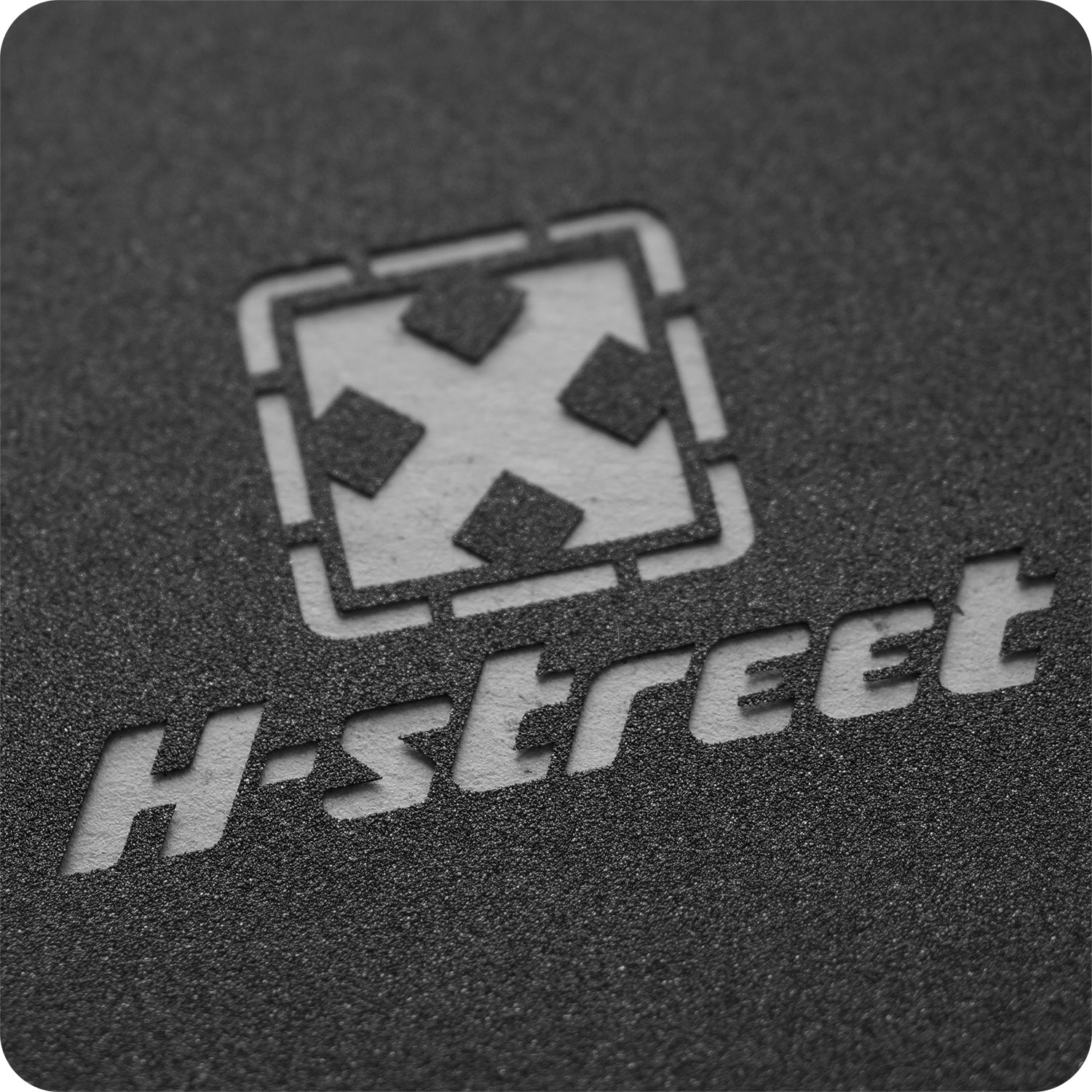 Close-up of Syndrome H-STREET DIECUT GRIPTAPE showing its textured black surface, die-cut square with four arrows logo, and bold, stylized H-street text.