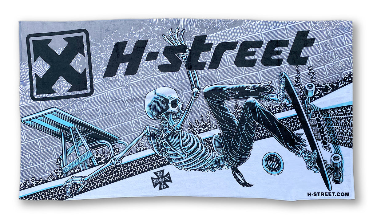 The Edith H-STREET DESIGNER TOWELS feature bold, digitally printed blue, black, and white graphics of a skeleton skateboarding in a pool with prominent "H-street" text and an X logo—perfect for the beach.