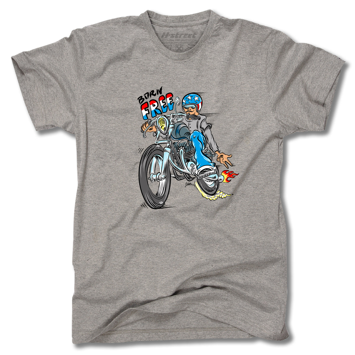 The Minuteman TONY MAG BORN FREE TEE is a grey shirt with a cartoon helmeted rider doing a wheelie, colorful "BORN FREE!" text above, and speedy flames—skateboard art inspired by Tony Mag.