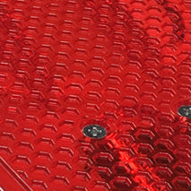 Close-up of the Mindtwister USA ZIPPY FLYER COMPLETE skateboard’s red, textured surface featuring a hexagonal pattern and two metallic screws, reflecting light—ideal for fun sidewalk surfing.